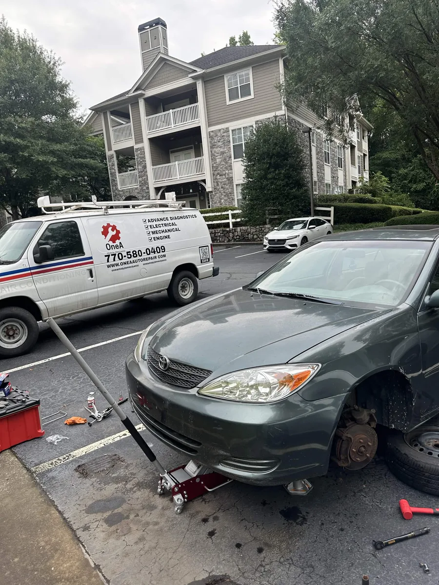 Toyota sedan with its front wheel removed beside the OneA service van